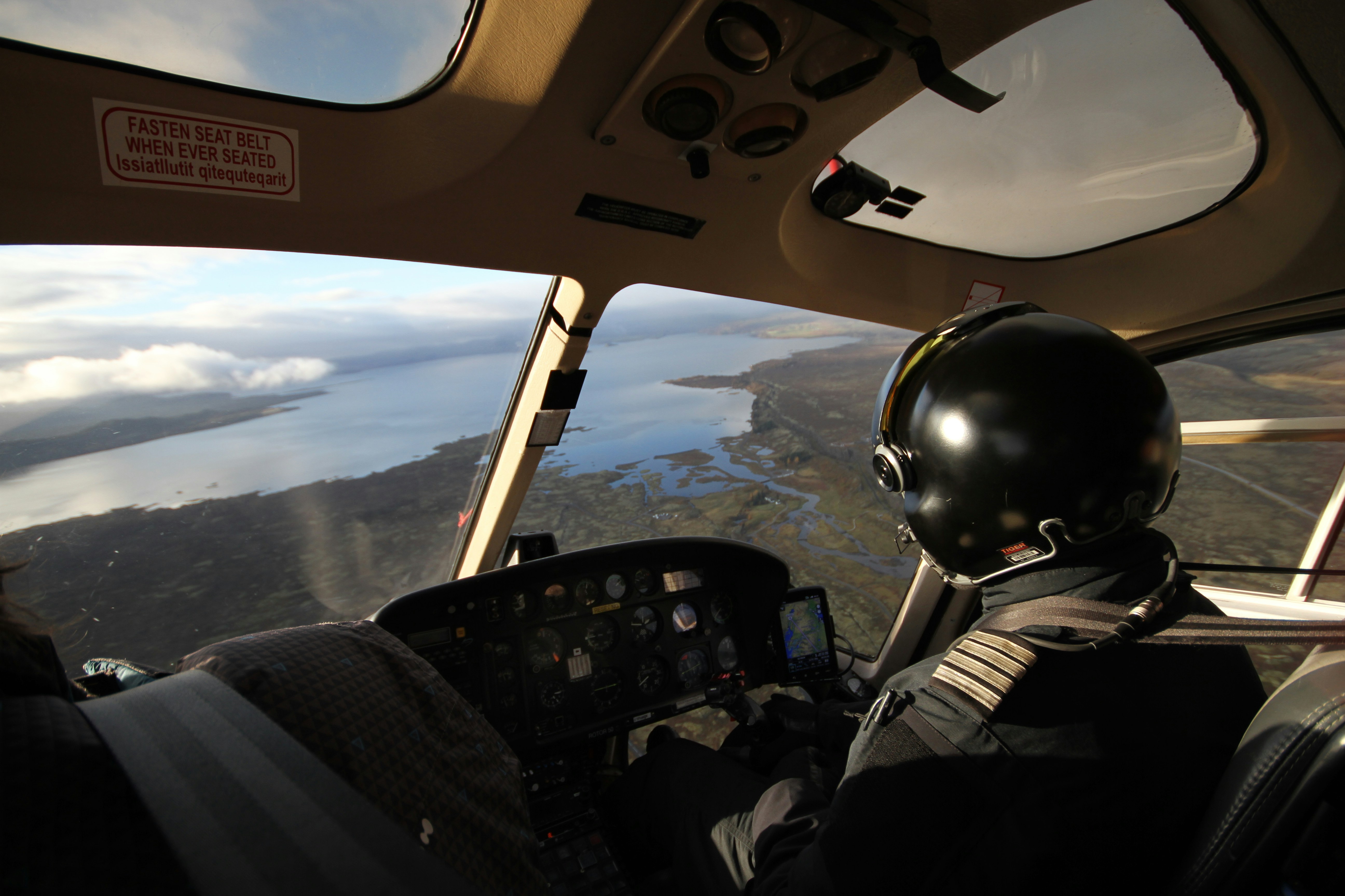 Professional helicopter pilot in full flight gear flying over a coastal wetland landscape
